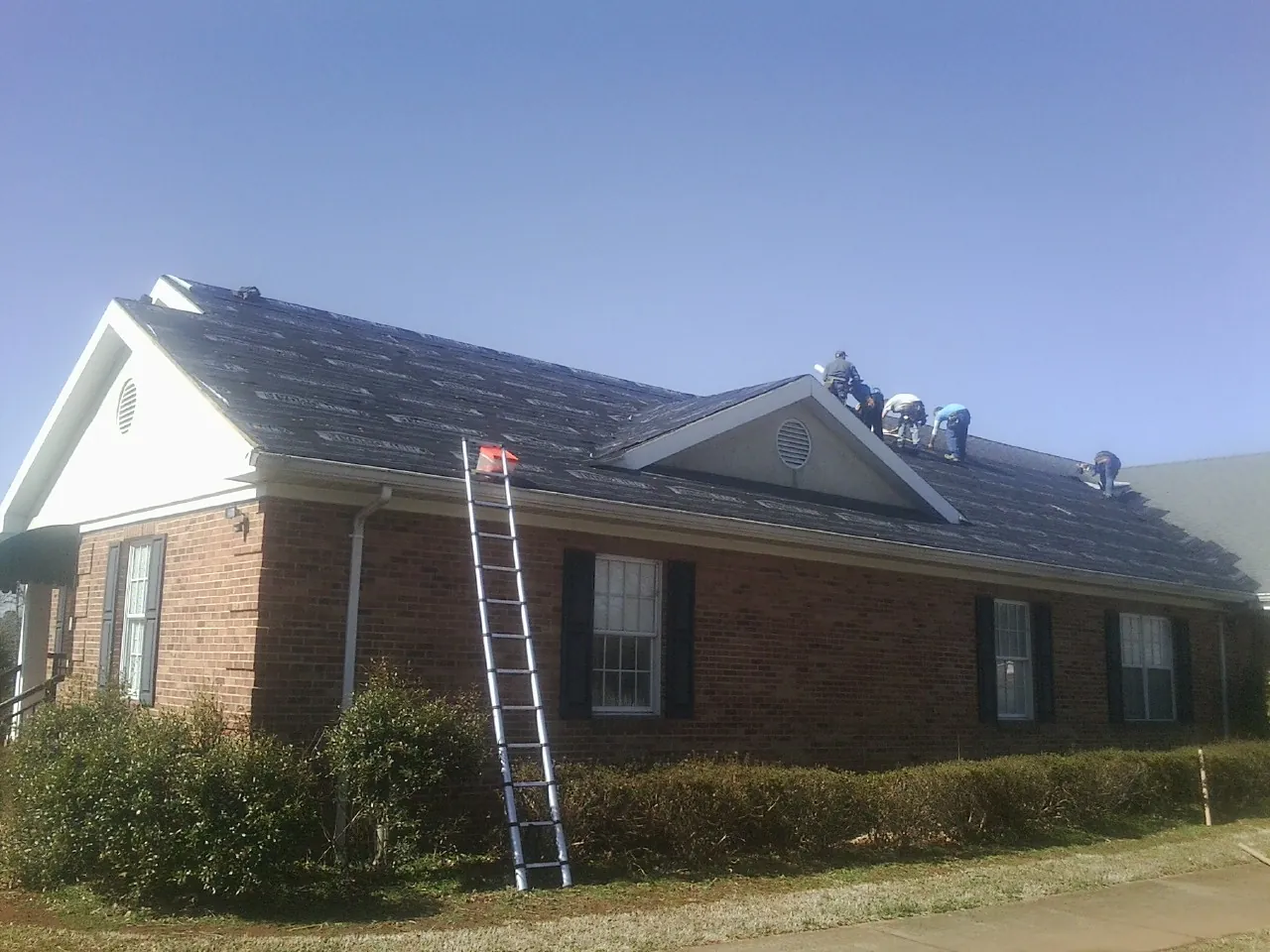 Crew tearing shingles off a brick ranch roof with a ladder set — Metal Roof Repair work by our crew in South Weymouth
