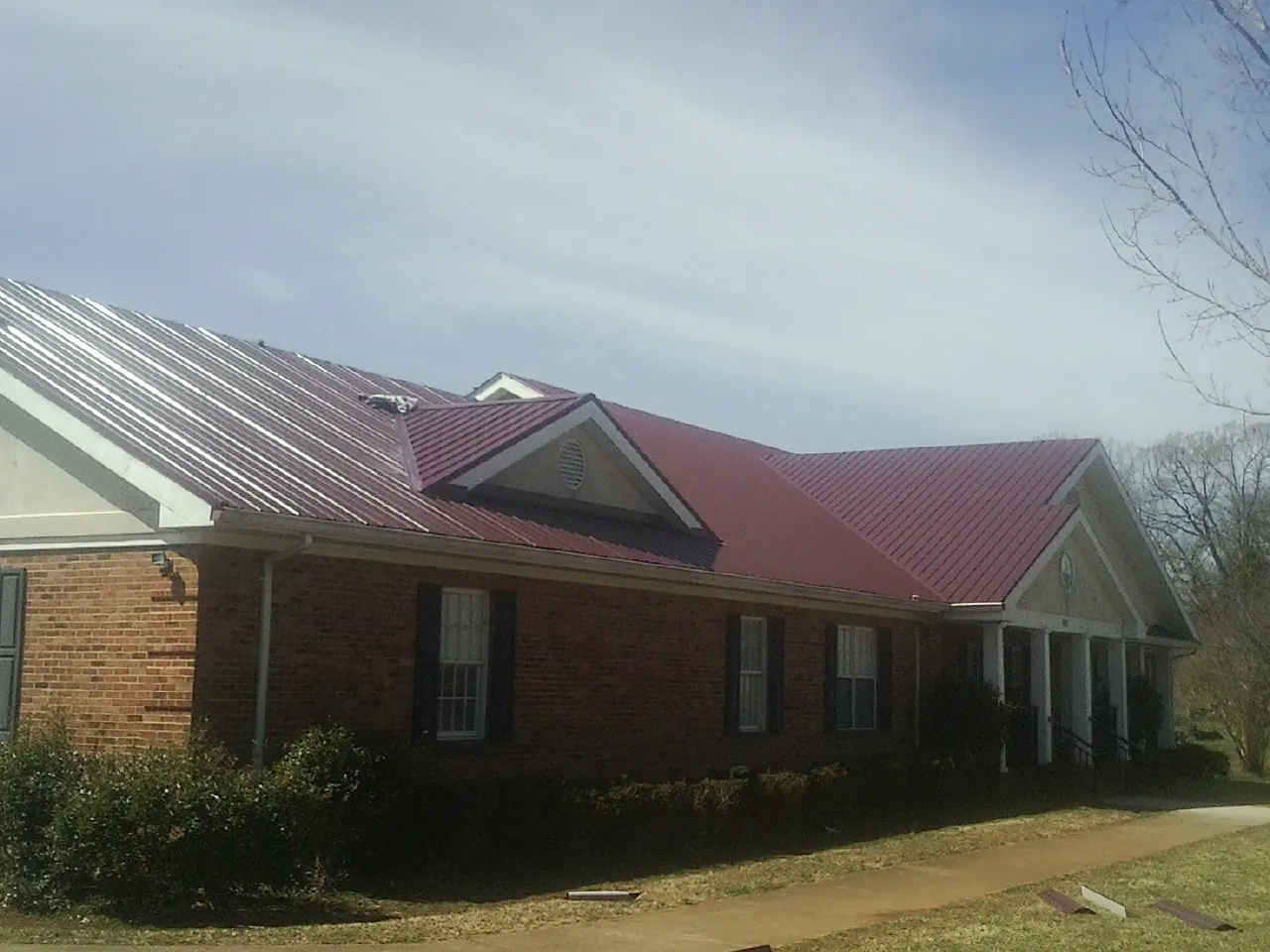 Red metal roof with gabled entries on a long brick building, from a Hail Damage Roof Repair job in South Weymouth
