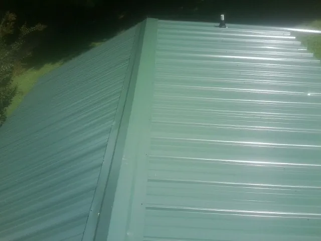 New green metal panels meeting at the ridge of a roof — Flat Roof Repair work by our crew in South Weymouth