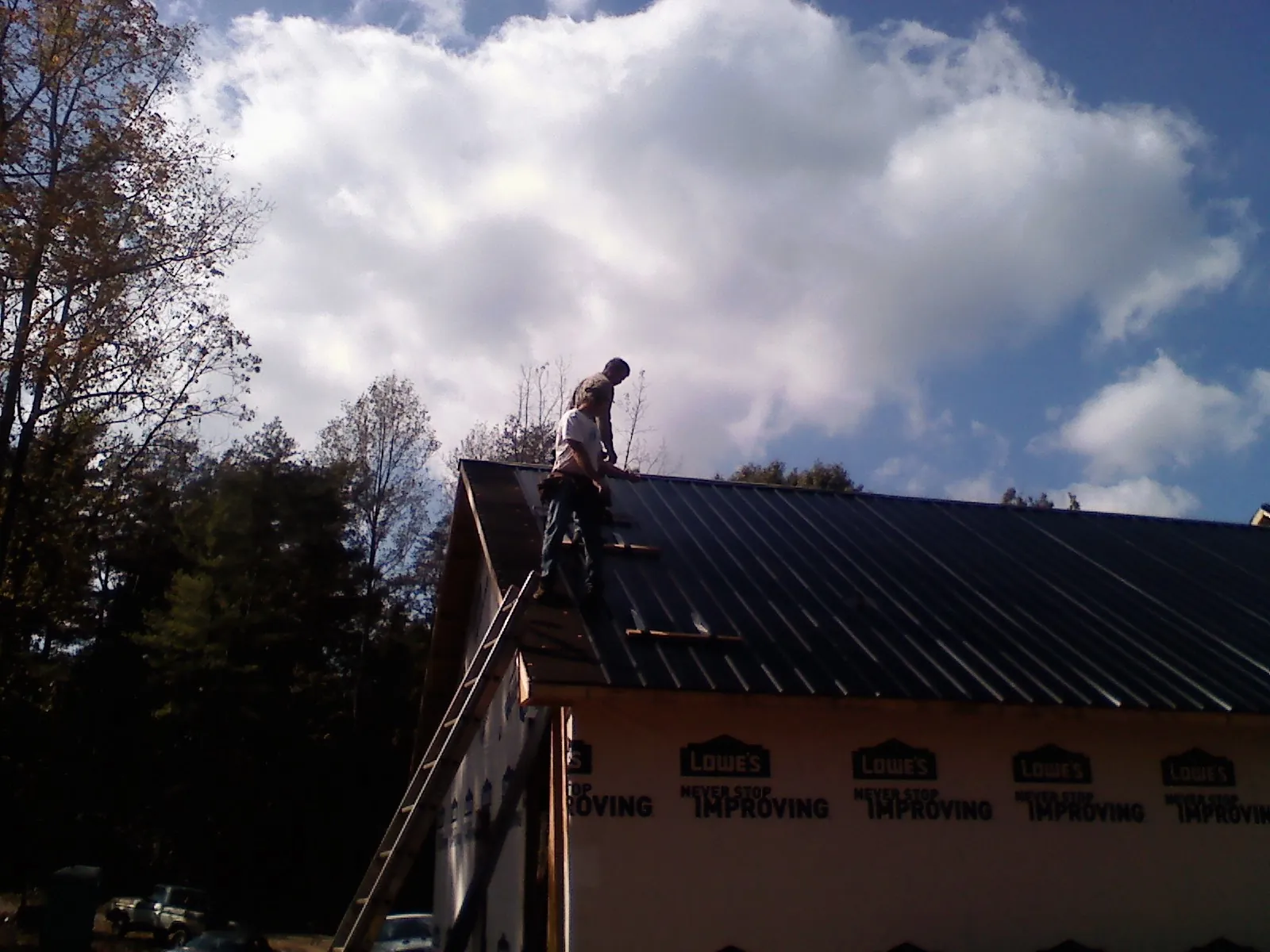 Roofer fastening dark metal panels high against a cloudy sky, from a Roof Inspection job in South Weymouth