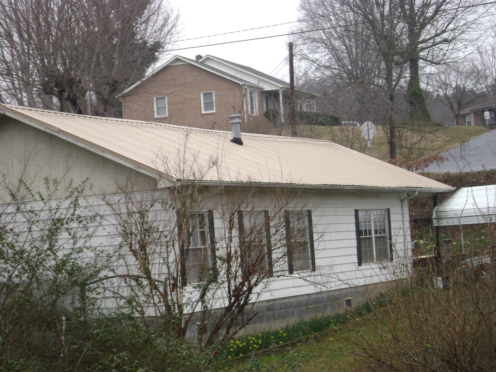 Tan metal roof on a white sided house set into a hillside — Commercial Roofing by Roofing Brothers in South Weymouth